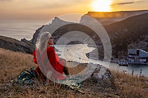 Woman sunset sea mountains. Happy woman siting with her back on the sunset in nature summer posing with mountains on