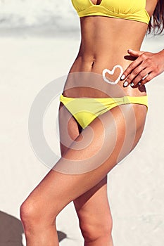 Woman with suntan lotion in form of the heart in yellow bikini.