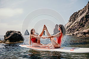 Woman sup yoga. Two happy sporty women practising yoga pilates on paddle sup surfboard. Female stretching doing workout