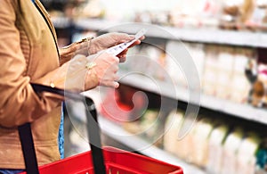 Woman in supermarket aisle with food shelf reading shopping list