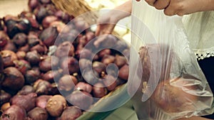 A woman in a supermarket on a vegetable shelf, buys vegetables and fruits. Man chooses red onion. Slow motion