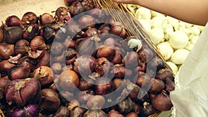 A woman in a supermarket on a vegetable shelf, buys vegetables and fruits. Man chooses red onion. Slow motion