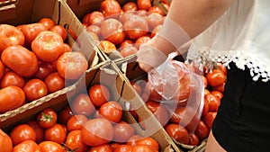 A woman in a supermarket on a vegetable shelf, buys vegetables and fruits. Man chooses a tomato, Slow motion