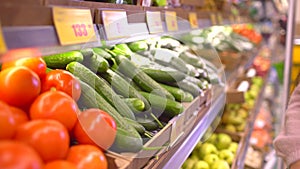 A woman in a supermarket on a vegetable shelf, buys vegetables and fruits. Woman chooses cucumbers. Slow motion.