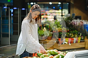Woman in a supermarket at the vegetable shelf shopping for groceries, she is choosing