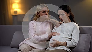 Woman supporting her upset pregnant friend, holding hand, single future mother