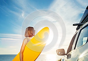 Woman with surf board by the car look on sunset over ocean