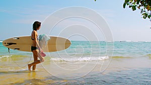 Woman with surfboard holds slates walking in ocean water
