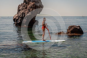 Woman surfboard the sea on a sunny summer day. In a red bathing suit stands with an oar. Summer fun by the sea