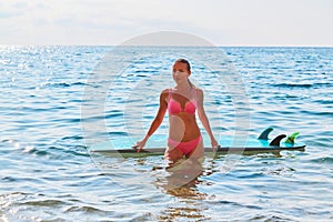 Woman surfer on beach. Pretty girl in bikini posing with surfboard in sea. Summer holidays concept. Extreme sport idea