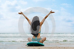 Woman surfer in bikini sitting on surfboard on beach in front of sea