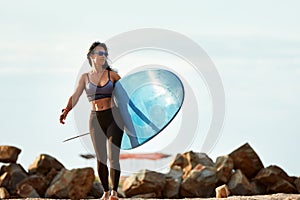 Woman surfer with surfboard going to surf at seaside. Girl holding surfboard o and goes to the ocean sea.