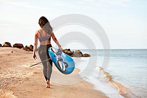 Woman surfer with surfboard going to surf at seaside. Girl holding surfboard o and goes to the ocean sea, a view from