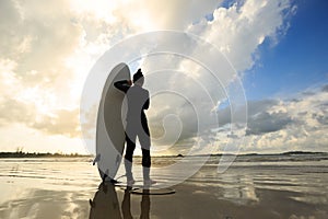 Woman surfer with surfboard on sunrise beach