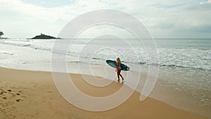 Woman surfer in swimsuit walks on beach holding surfboard by ocean aerial view. Young caucasian female in bikini carries