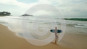 Woman surfer in swimsuit walks on beach holding surfboard by ocean aerial view. Young caucasian female in bikini carries