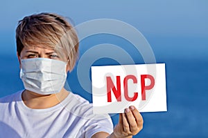 Woman in surgical face mask holds blank with text NCP that mean Novel Coronavirus Pneumonia