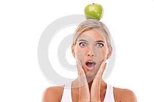 Woman, surprise and apple on head in studio for wellness, nutrition and balance by white background. Isolated model