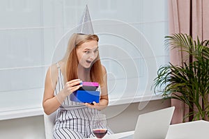 Woman with a surprised face holds gift in her hands. Birthday during a pandemic.