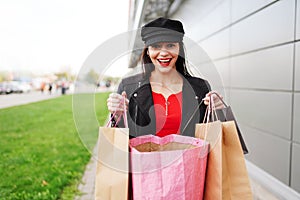 Woman with surprised face and shopping bags on city street. Female walking outdoors in black clothes