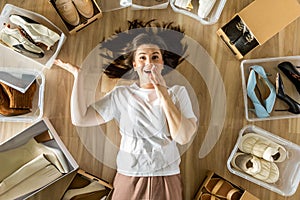 Woman surrounded by shoes in plastic container and cardboard box shopaholism and storage organizing photo
