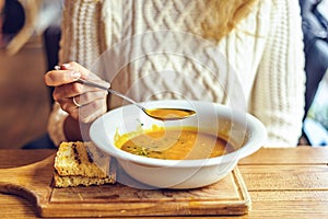 Woman in sweater eating dry pea soup on wooden platter