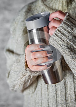 Woman in a sweater holds a thermomug with a hot drink in her hands