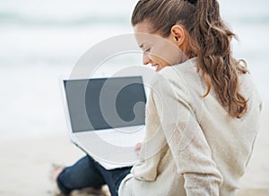 Woman in sweater sitting on lonely beach and using laptop