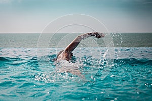 Woman swimming crawl style in a pool with sea view and blue sky