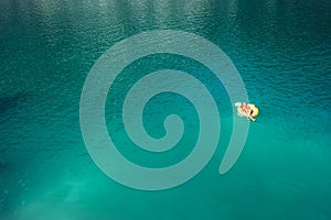 Woman swimming on inflatable pineapple ring in mountain lake top aerial view. Carefree vacation lifetime concept image