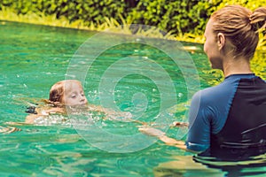 Woman swimming instructor for children is teaching a happy boy to swim in the pool