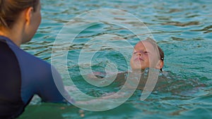 Woman swimming instructor teaches little boy swimming in a sea during a sundet