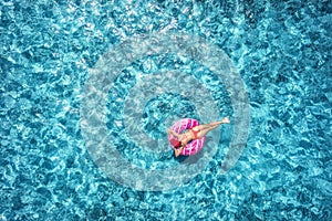 Woman swimming on pink donut swim ring in blue sea. Aerial view