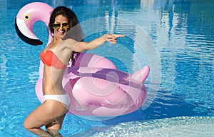 Woman in a swimming pool leisure on a giant inflatable giant pink flamingo float mattress in red bikini