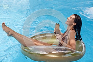 Woman in swimming pool on rubber ring relaxing while having vacation, enjoying summer season, spending time drinking fresh