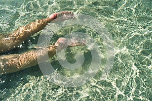 Woman swimming on the sea. Female legs under clear sea water. Realistic top view photo of a women's legs barefoot.