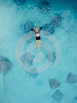 Woman swimming with stingrays in Maldives. Sting ray fishes and woman swimming in blue sea, Aerial view