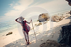 Woman in swimming suit on the beach with hat, stick and backpack