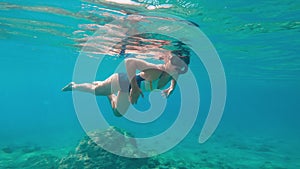 Woman in a swimming suit freediving at the depth of the sea.