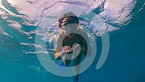 A woman is swimming underwater and looking at the camera