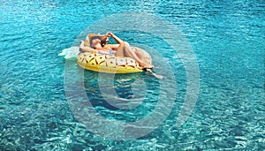 Woman swims on inflatable pineapple ring in the clear sea water.
