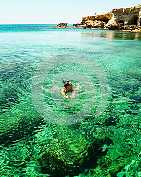 Woman swims in Northern cyprus Ayia napa bay shore with crystal clear blue mediterranean waters and tranquil seascape and rocky