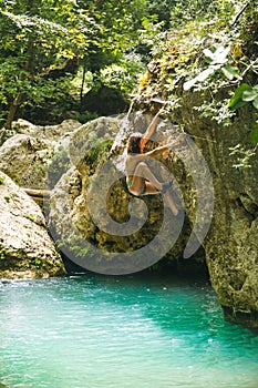 A woman in a swimsuit climbs a cliff above the water