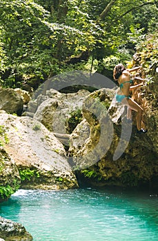 A woman in a swimsuit climbs a cliff above the water