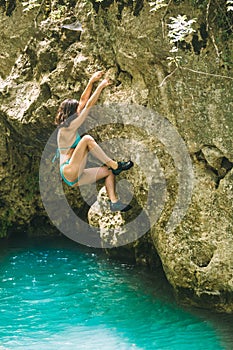 A woman in a swimsuit climbs a cliff above the water