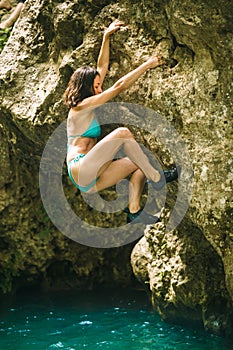 A woman in a swimsuit climbs a cliff above the water