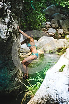 A woman in a swimsuit climbs a cliff above the water