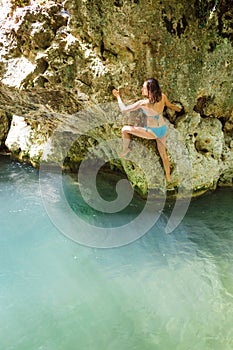 A woman in a swimsuit climbs a cliff above the water