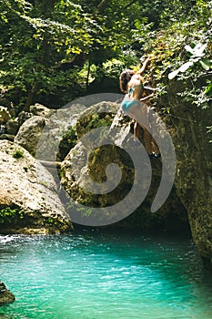 A woman in a swimsuit climbs a cliff above the water