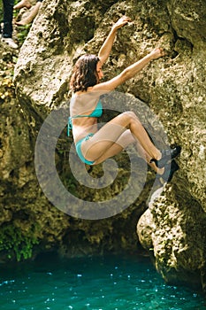 A woman in a swimsuit climbs a cliff above the water